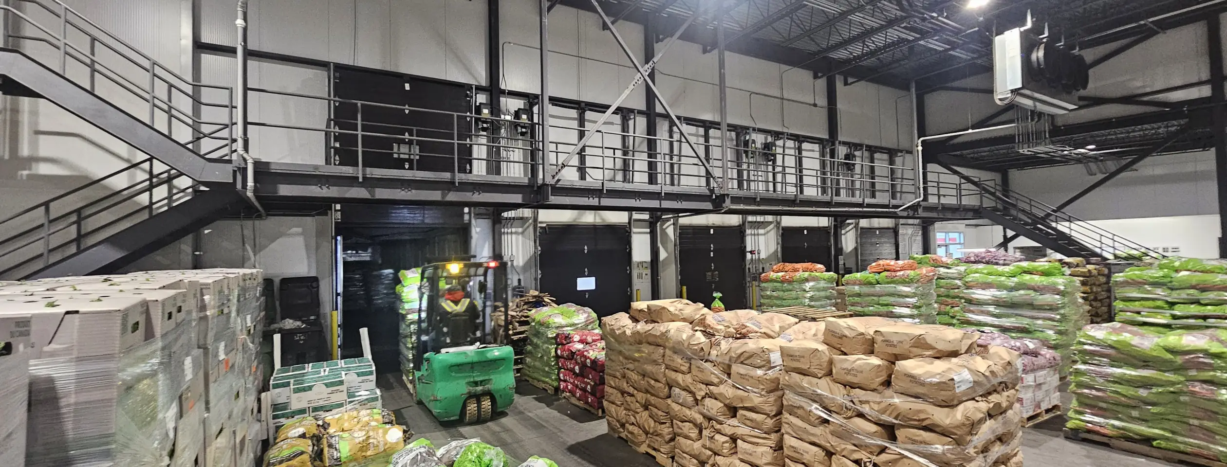 Forklift loading a trailer at an open dock door in a produce warehouse, pallets of potatoes and vegetables on the floor