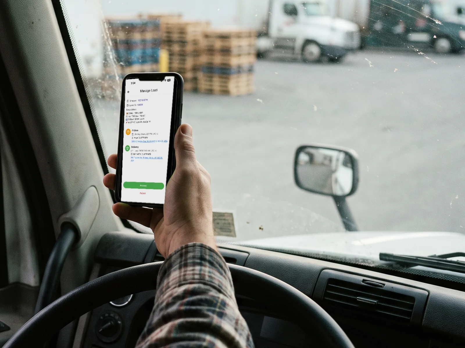 Truck driver holding a smartphone in the cab with the ShipLocate Driver app displaying a load assignment